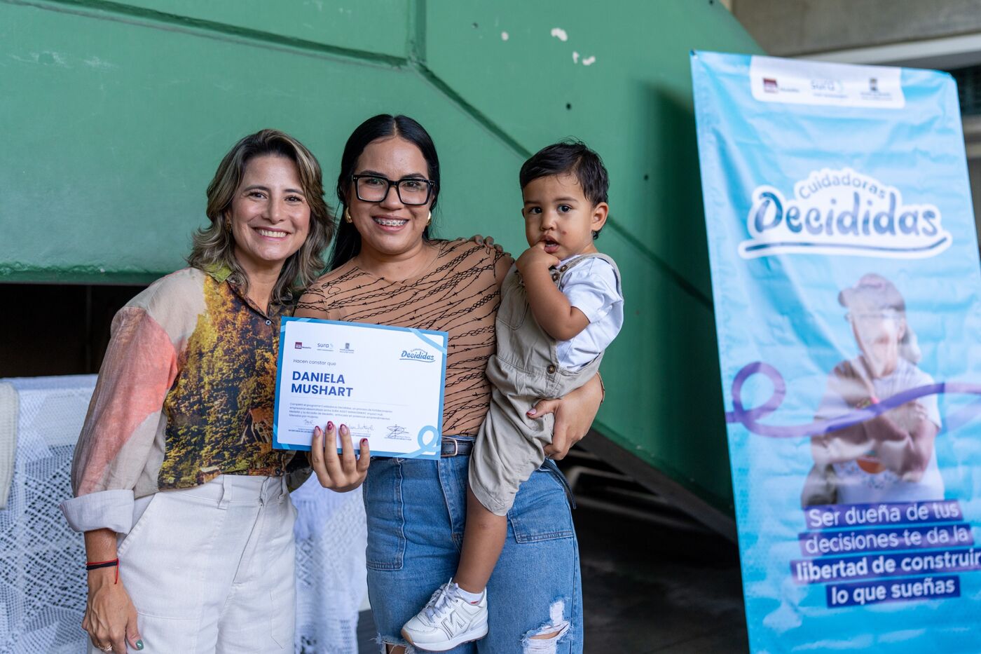 Una participante con su hijo en brazos recibe su certificado